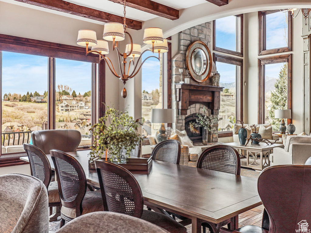 Dining area with a wealth of natural light, beam ceiling, a notable chandelier, and a stone fireplace