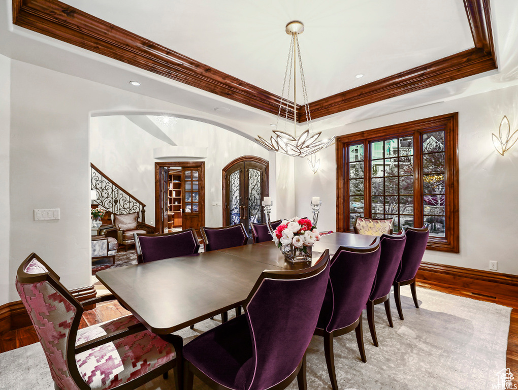 Dining room featuring french doors, a raised ceiling, ornamental molding, and wood finished floors