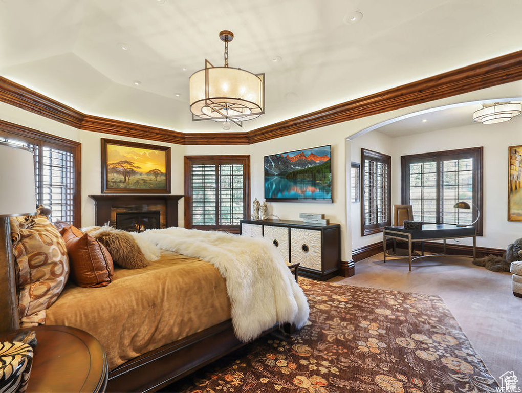 Bedroom with crown molding, an inviting chandelier, baseboards, arched walkways, and a warm lit fireplace