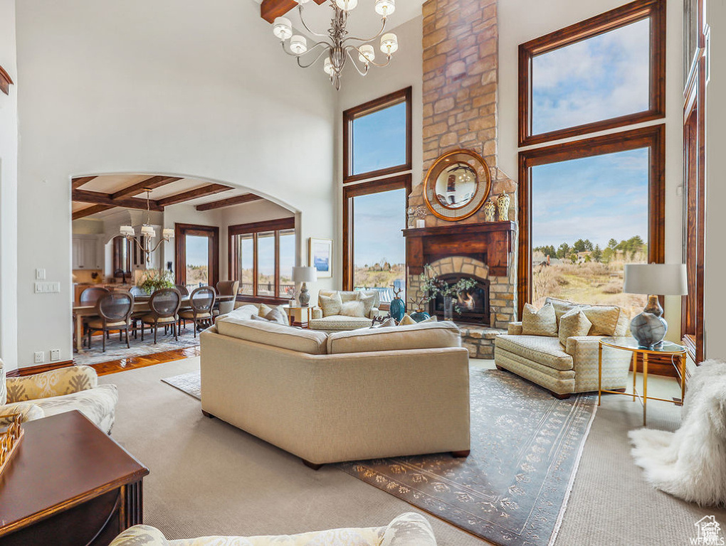 Living area featuring a large fireplace, beamed ceiling, arched walkways, a high ceiling, and an inviting chandelier