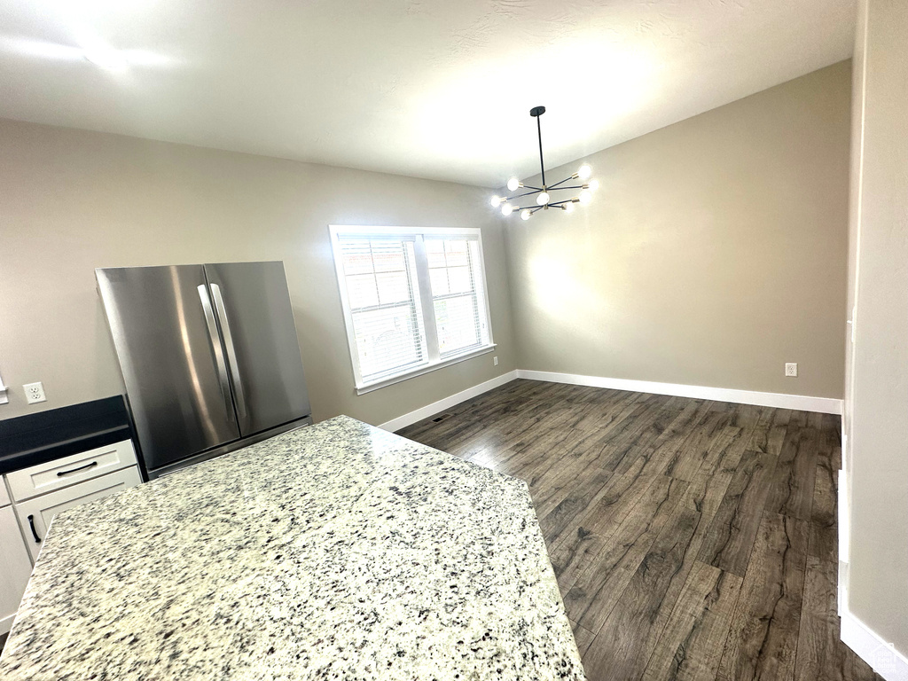 Kitchen featuring freestanding refrigerator, a chandelier, dark wood-type flooring, baseboards, and white cabinets
