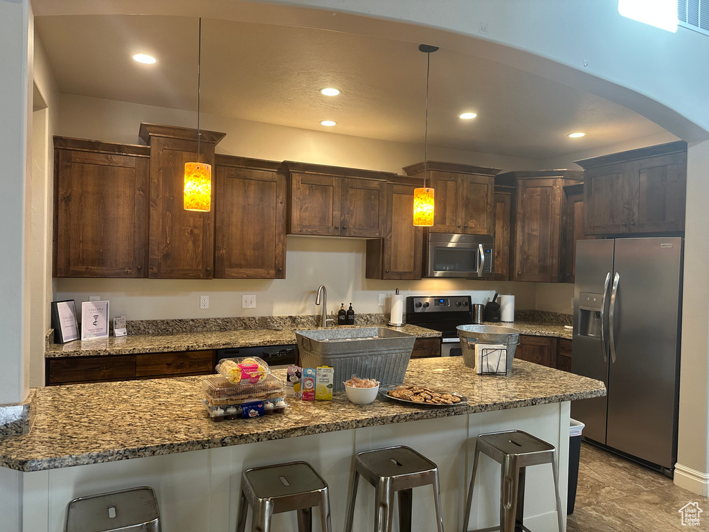 Kitchen featuring appliances with stainless steel finishes, a breakfast bar, recessed lighting, dark brown cabinetry, and stone countertops