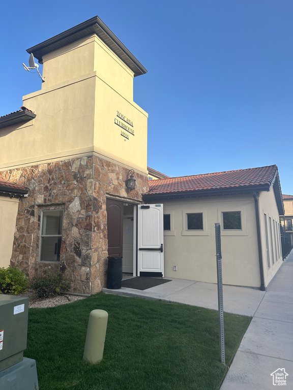 Rear view of property featuring a tiled roof, a yard, stone siding, and stucco siding