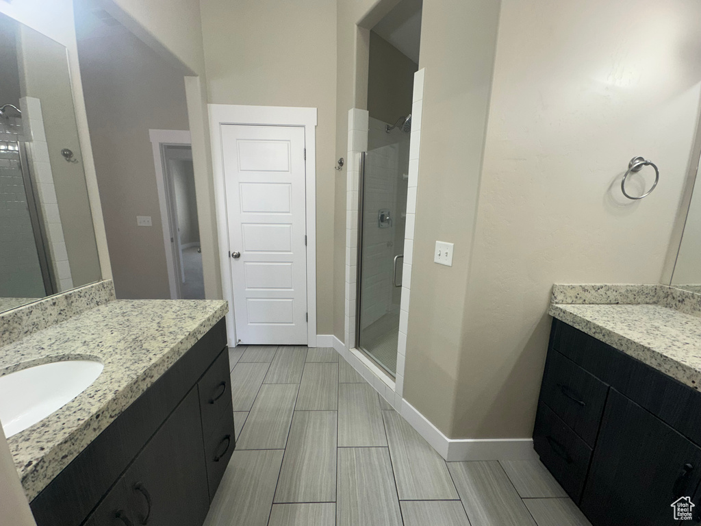 Full bath featuring a shower stall, two vanities, and baseboards