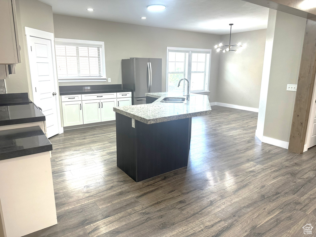 Kitchen with a sink, freestanding refrigerator, baseboards, a chandelier, and a center island with sink