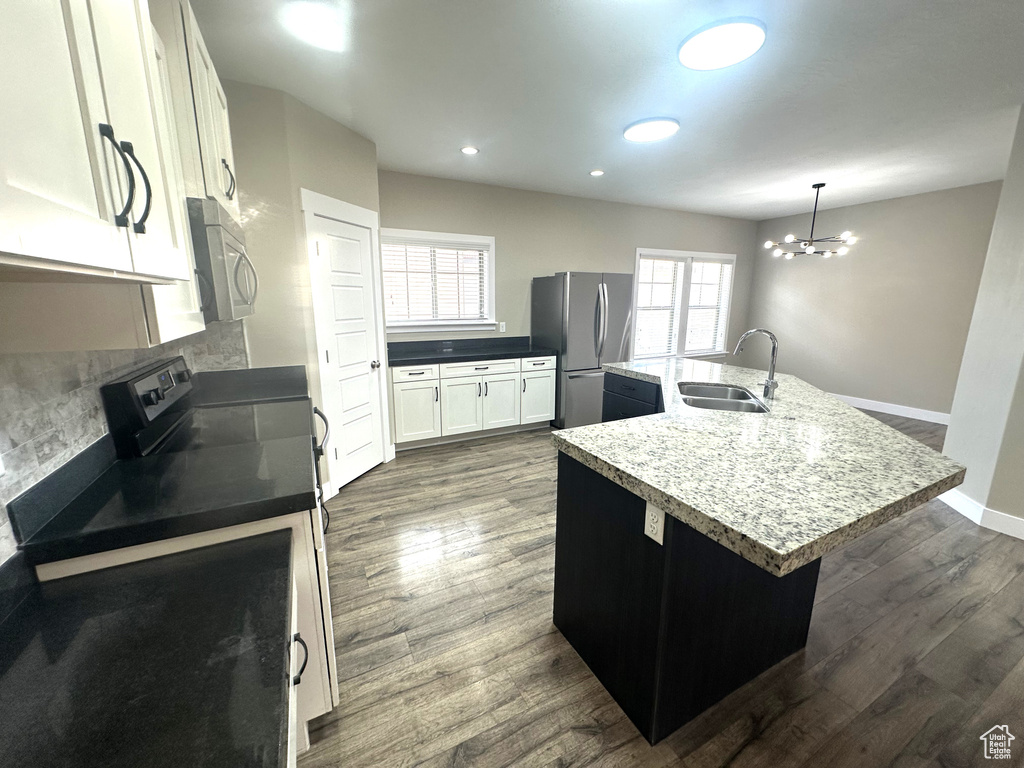 Kitchen with a sink, appliances with stainless steel finishes, a kitchen island with sink, backsplash, and dark wood-style floors