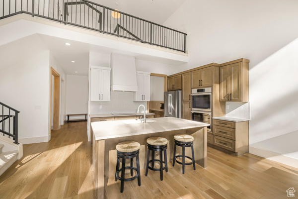 Kitchen featuring stainless steel appliances, a high ceiling, a breakfast bar, light wood finished floors, and light countertops