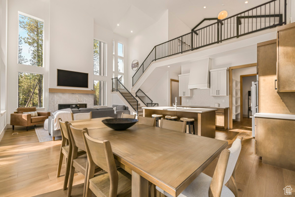 Dining space featuring a towering ceiling, stairs, light wood finished floors, a fireplace, and recessed lighting