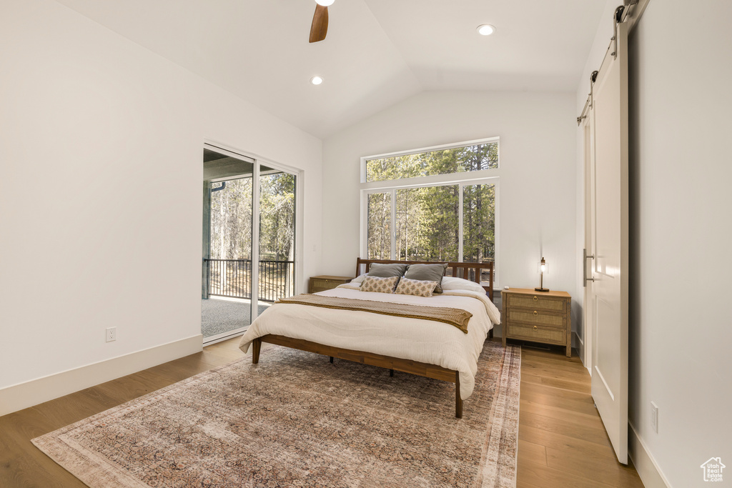 Bedroom with a barn door, access to exterior, multiple windows, lofted ceiling, and light wood-style flooring