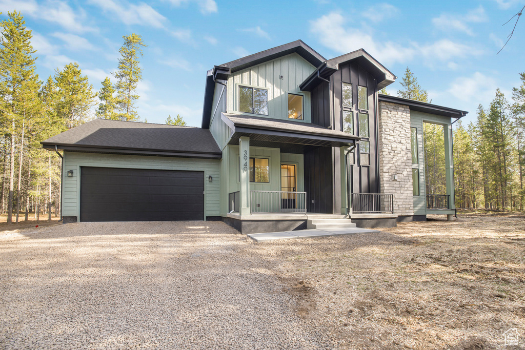 View of front facade featuring gravel driveway, covered porch, and an attached garage