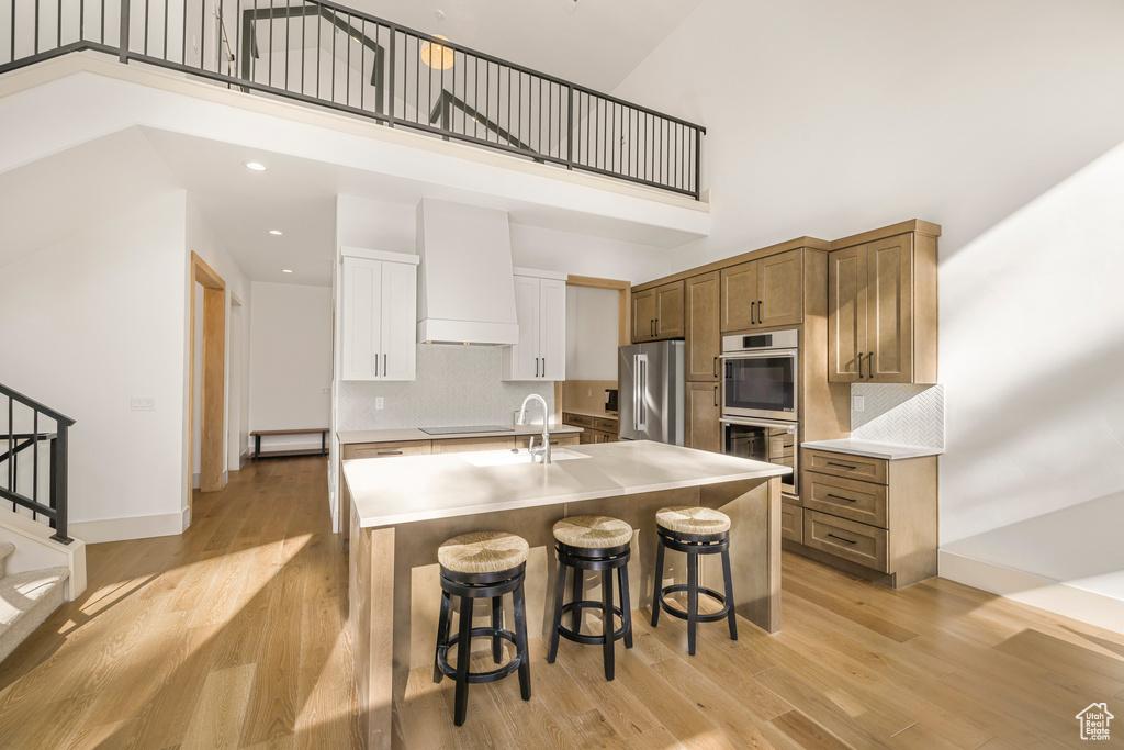 Kitchen with stainless steel appliances, a high ceiling, a kitchen bar, light wood-style flooring, and light countertops