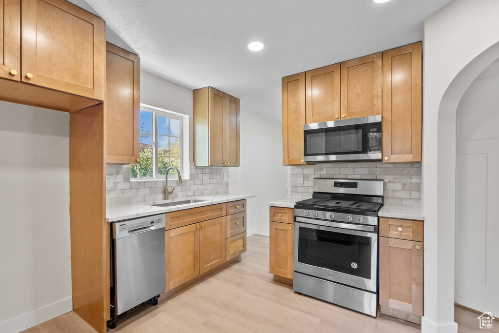 Kitchen with appliances with stainless steel finishes, a sink, light wood-type flooring, light countertops, and recessed lighting