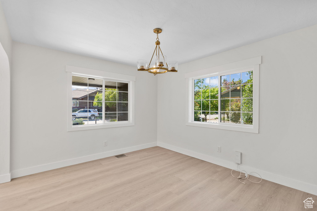 Unfurnished room with plenty of natural light, a chandelier, wood finished floors, and baseboards