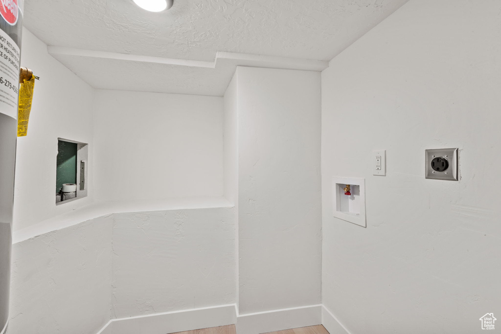 Laundry area with hookup for a washing machine, electric dryer hookup, light wood-style floors, a textured ceiling, and baseboards