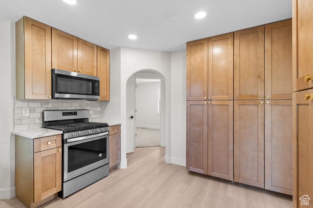 Kitchen with appliances with stainless steel finishes, light wood-style floors, arched walkways, decorative backsplash, and recessed lighting