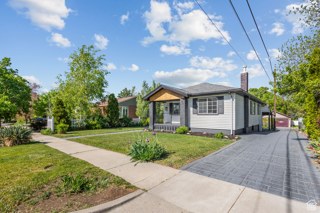 View of front of home with a front yard, covered porch, a chimney, and an outdoor structure