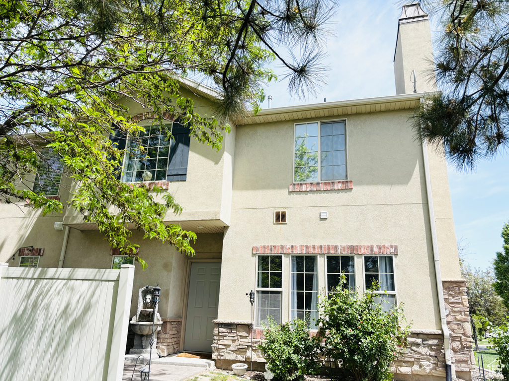 Back of house with stucco siding, stone siding, and fence