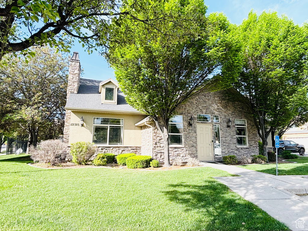 View of front of house featuring stone siding, a front lawn, stucco siding, and a chimney