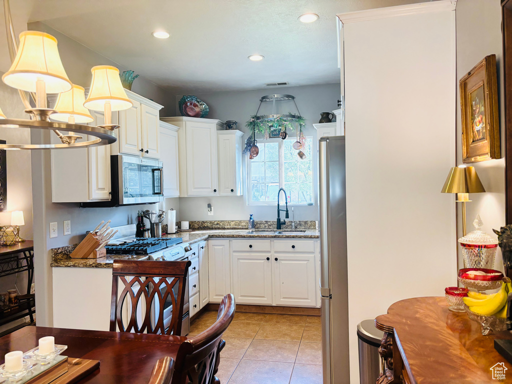 Kitchen with appliances with stainless steel finishes, a sink, white cabinets, light tile patterned floors, and recessed lighting