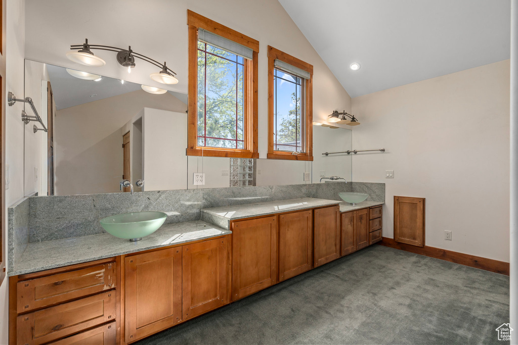 Bathroom featuring vaulted ceiling, double vanity, and baseboards