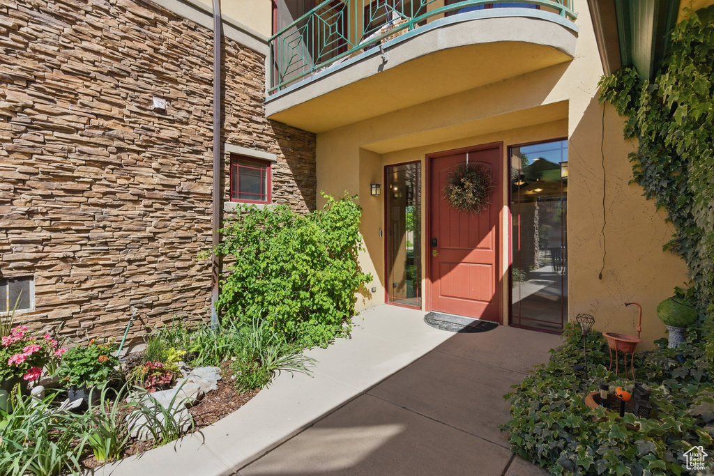 Entrance to property featuring a balcony, stone siding, and stucco siding