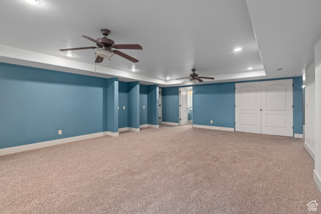 Unfurnished living room featuring a tray ceiling, recessed lighting, ceiling fan, light carpet, and baseboards