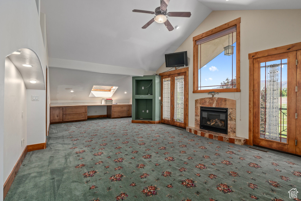 Unfurnished living room featuring carpet flooring, a ceiling fan, a fireplace, baseboards, and a desk
