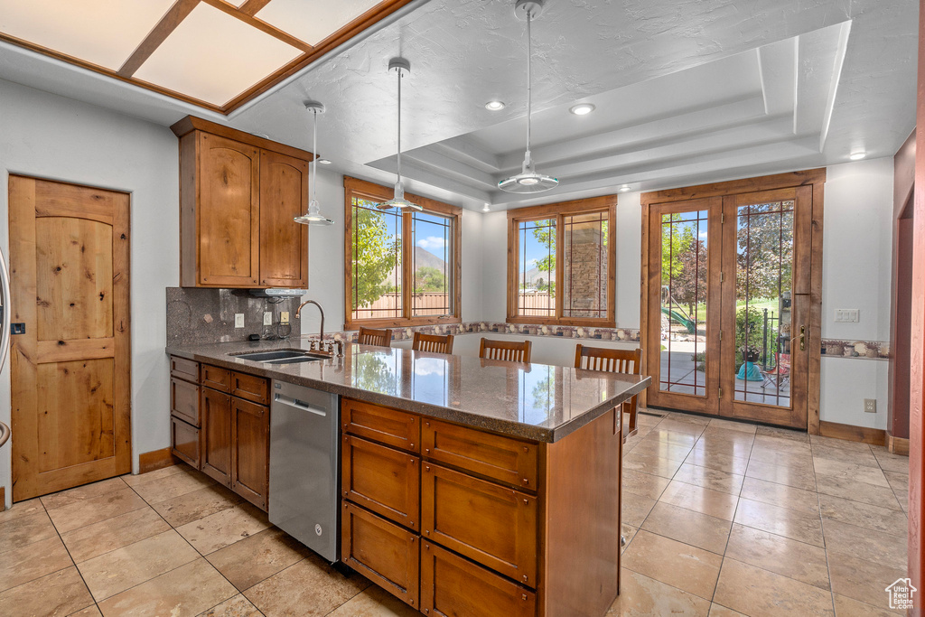 Kitchen featuring stainless steel dishwasher, a sink, a peninsula, a raised ceiling, and brown cabinetry