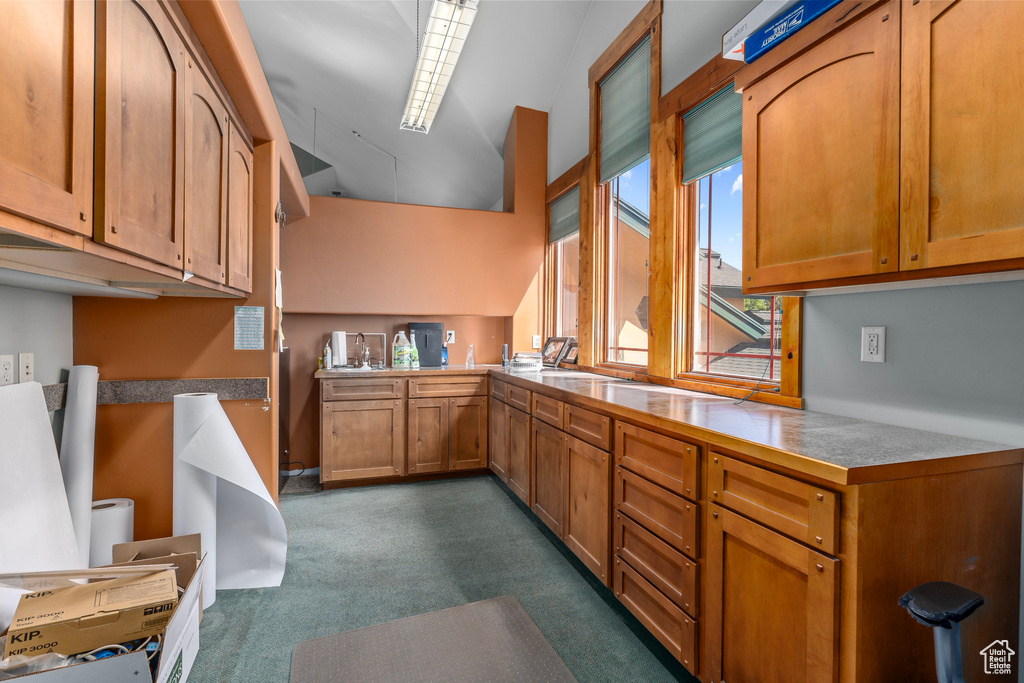 Kitchen with dark colored carpet, brown cabinets, and lofted ceiling