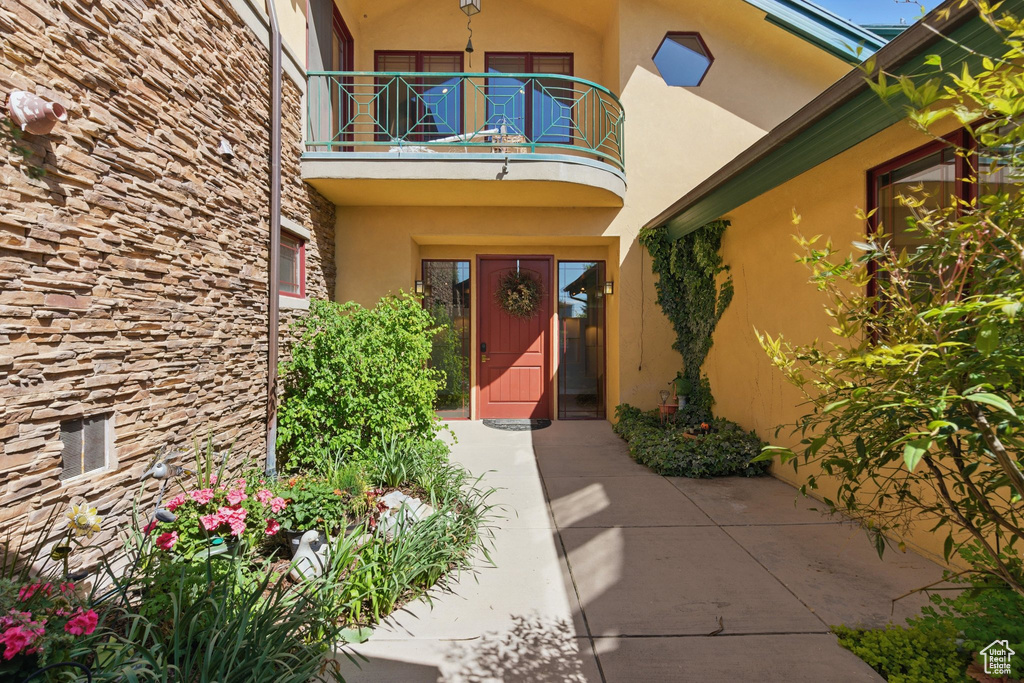 Doorway to property with a balcony, stucco siding, and stone siding