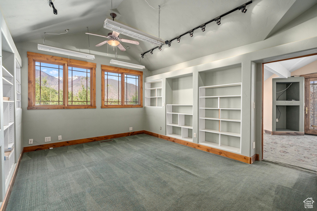 Carpeted empty room featuring rail lighting, vaulted ceiling, a ceiling fan, baseboards, and built in features