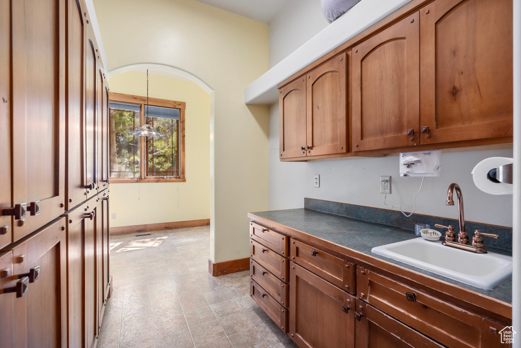 Kitchen featuring a sink, dark countertops, pendant lighting, baseboards, and brown cabinetry