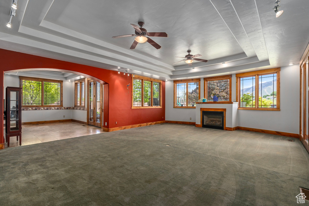 Unfurnished living room with a raised ceiling, arched walkways, baseboards, ceiling fan, and carpet floors