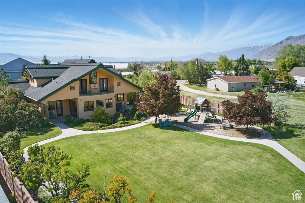 View of front of home featuring a playground, a balcony, a front yard, a mountain view, and stucco siding