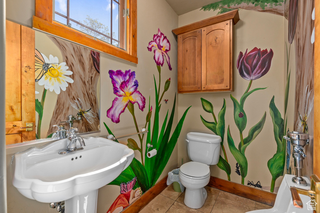 Bathroom featuring toilet, a sink, baseboards, and tile patterned flooring