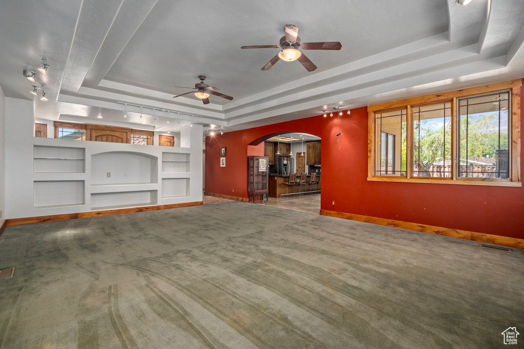 Unfurnished living room with a tray ceiling, arched walkways, baseboards, built in shelves, and ceiling fan