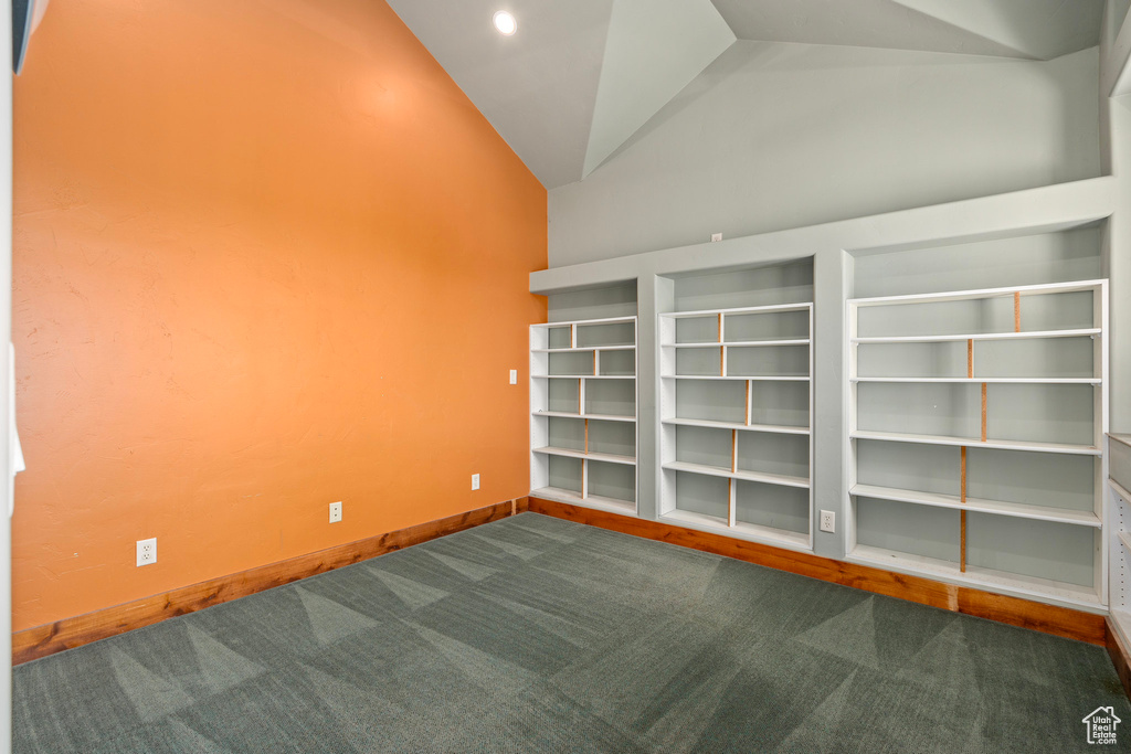 Unfurnished room featuring dark colored carpet, lofted ceiling, and baseboards