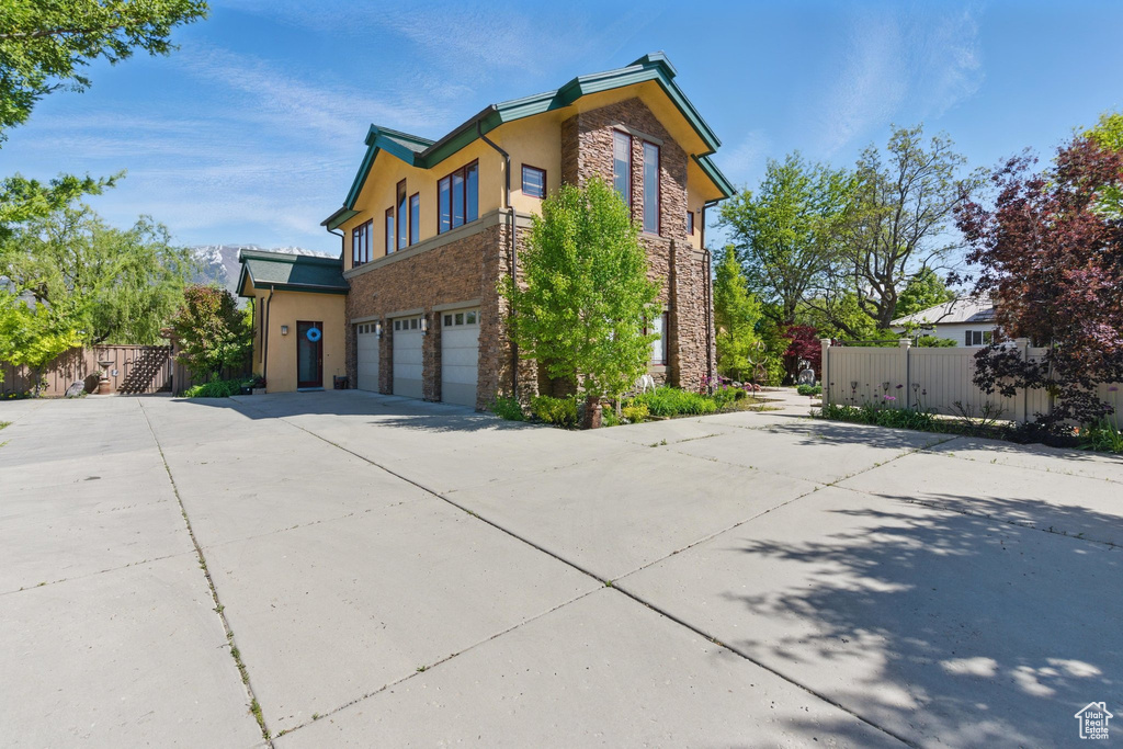 View of home\'s exterior featuring stone siding, a garage, concrete driveway, fence, and stucco siding