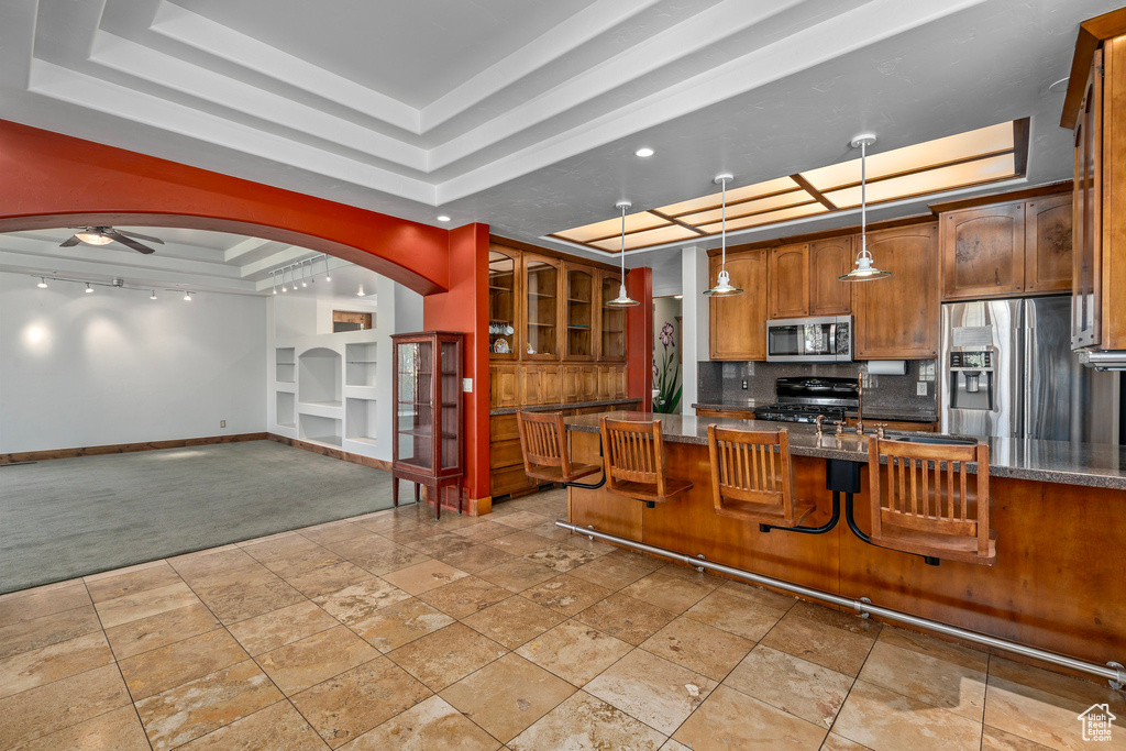 Kitchen featuring stainless steel appliances, a tray ceiling, baseboards, brown cabinetry, and built in features