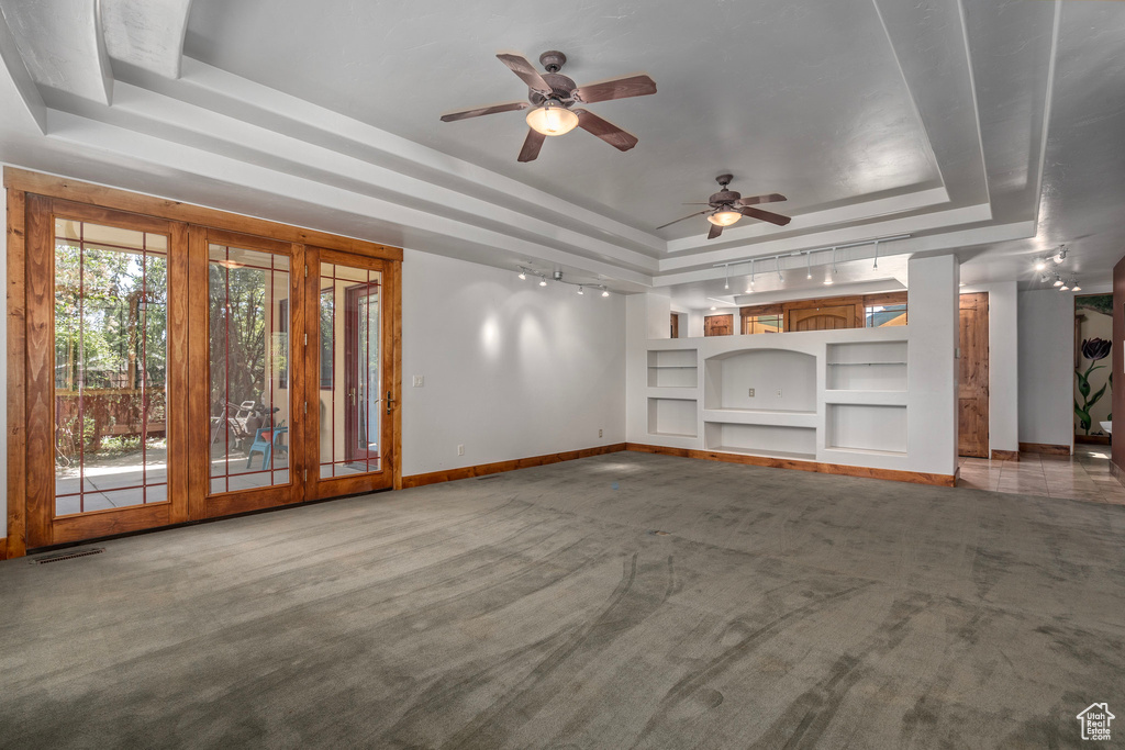 Unfurnished living room with a raised ceiling, carpet floors, built in shelves, baseboards, and ceiling fan