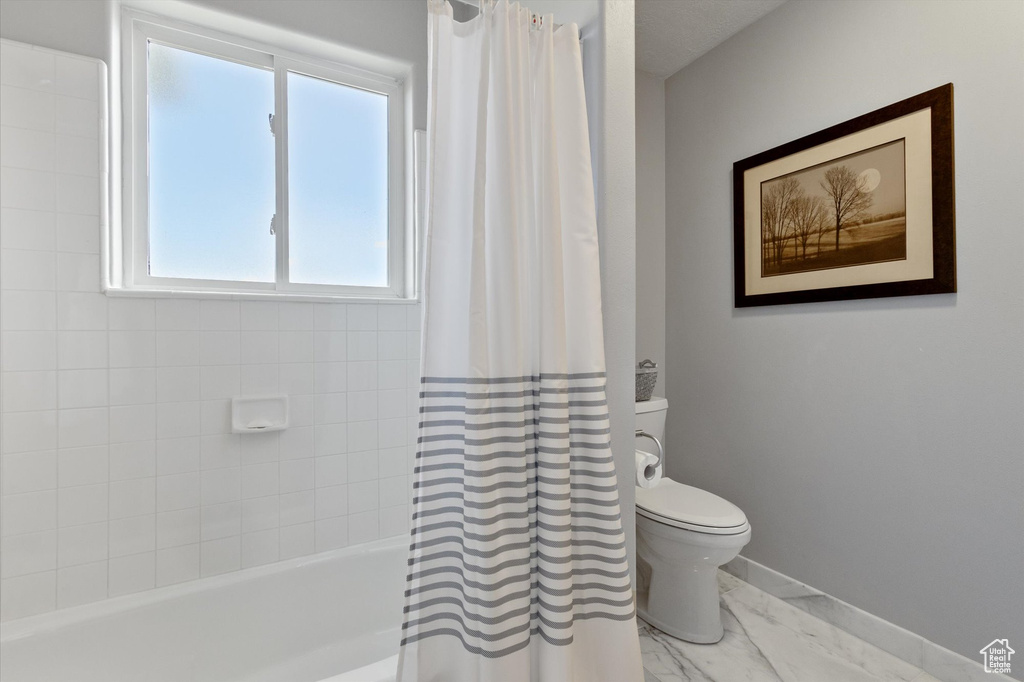 Full bath with marble look tile flooring, toilet, baseboards, and shower / bath combination with curtain