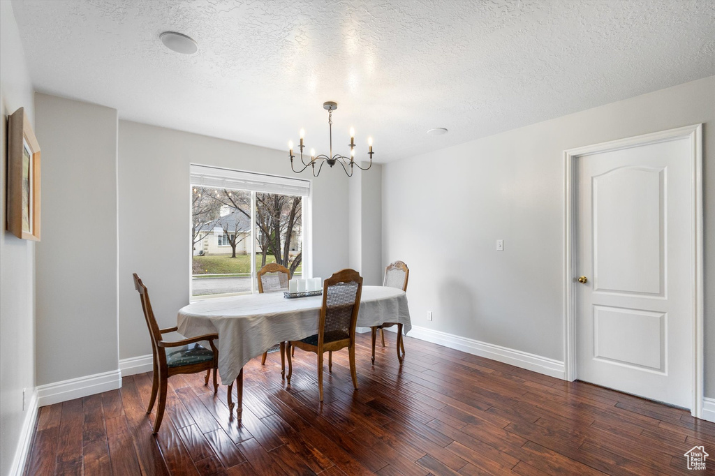 Dining area featuring a chandelier, dark wood-style flooring, baseboards, and a textured ceiling