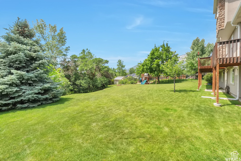 View of green lawn featuring a playground and a deck