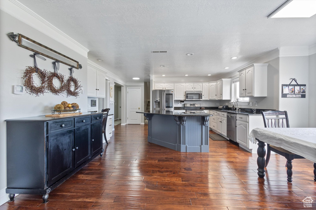 Kitchen with appliances with stainless steel finishes, dark countertops, white cabinets, crown molding, and dark wood-style flooring
