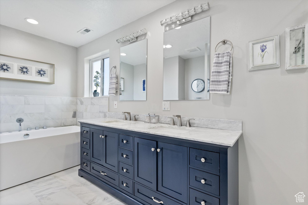 Full bathroom featuring marble finish floors, a freestanding bath, double vanity, and recessed lighting