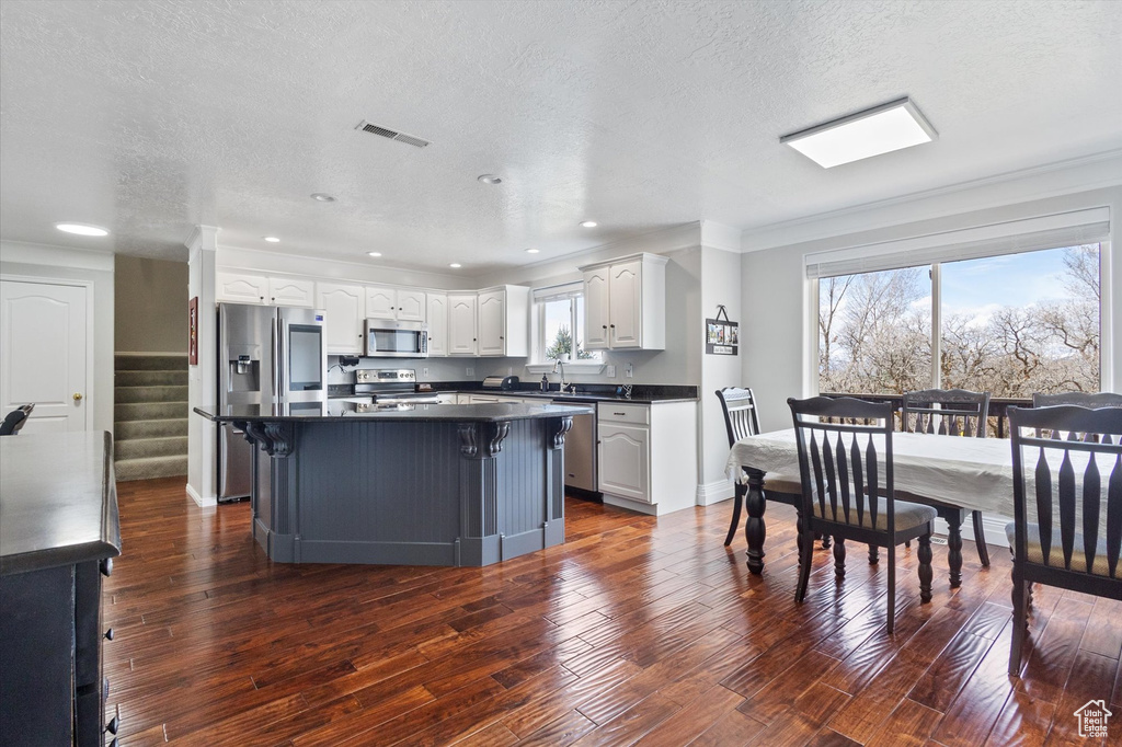 Kitchen featuring appliances with stainless steel finishes, dark countertops, white cabinetry, a textured ceiling, and dark wood-style floors