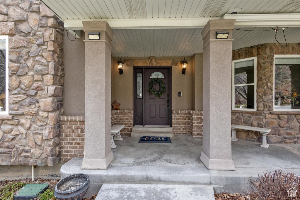 Doorway to property featuring stone siding, stucco siding, and a porch