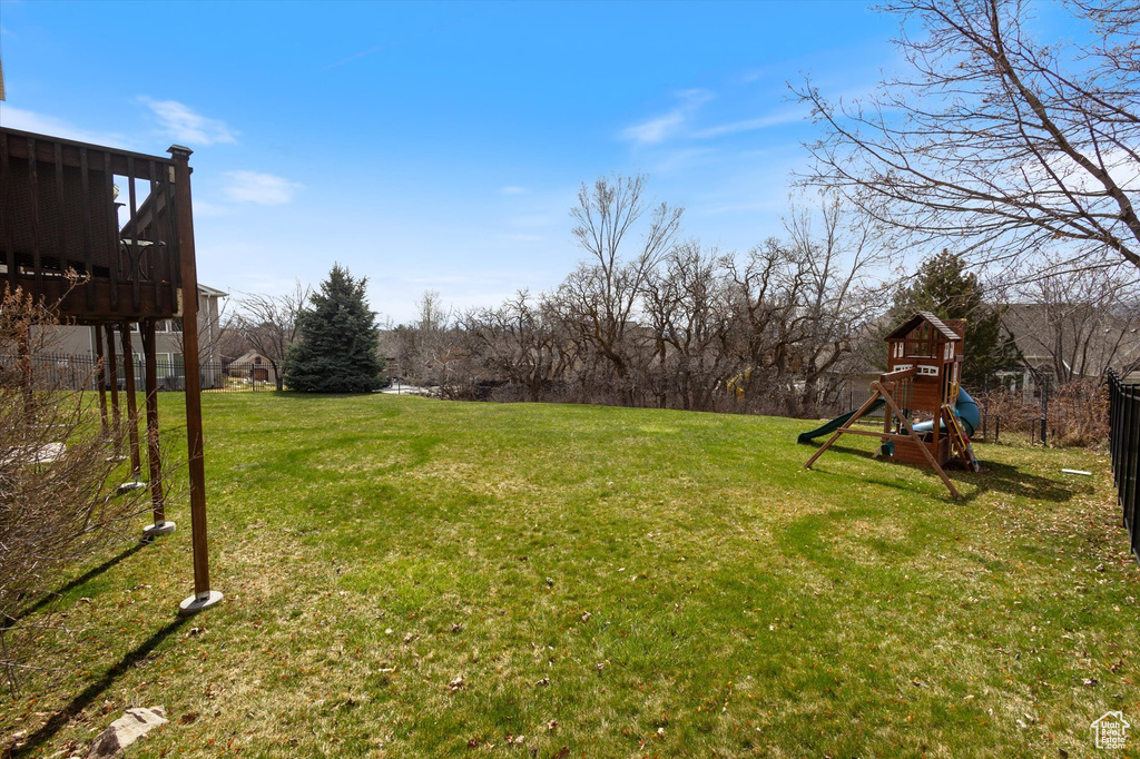 View of grassy yard featuring a playground and a wooden deck