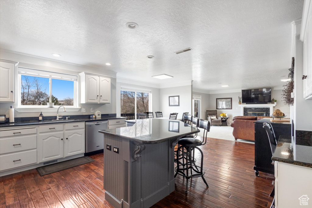 Kitchen featuring dishwasher, ornamental molding, a kitchen island, a breakfast bar, and white cabinetry