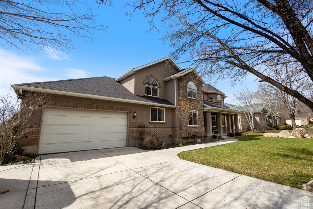 Traditional home with stucco siding, driveway, a front yard, an attached garage, and stone siding